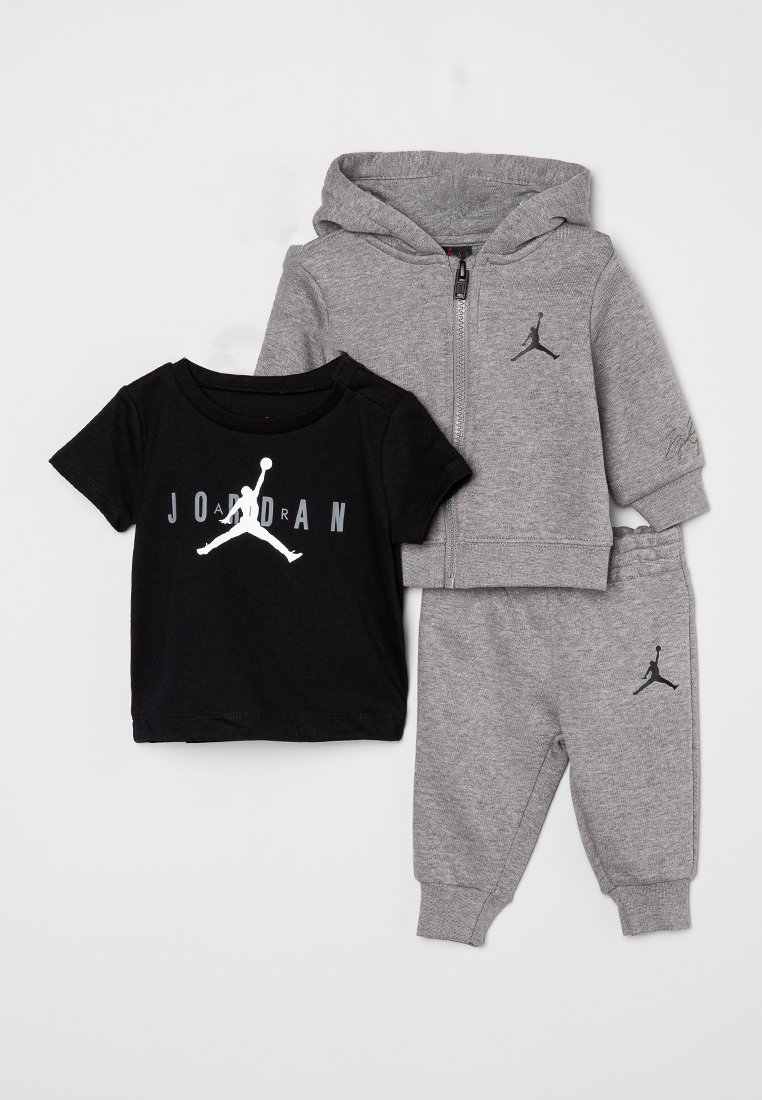 Ensemble pour tout-petit Jordan comprenant un t-shirt noir avec logo, un sweat à capuche gris avec zip, et un pantalon de survêtement gris assorti, le tout en matières douces.