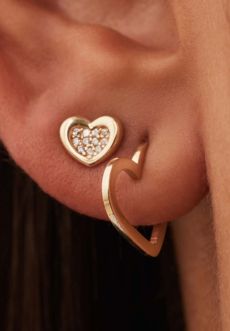 Boucles d'oreilles en ton or en forme de cœur, présentant un design de cœur solide avec un petit cœur incrusté, orné de petites pierres claires et affichant une finition polie.
