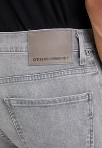 Šedé denimové džíny s koženou nášivkou s nápisem "CITIZENS of HUMANITY", s zadními kapsami a jemnou texturou.