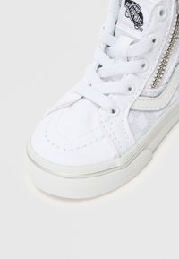 Sneaker alta in tela bianca con cuciture tono su tono, accenti laterali testurizzati e dettaglio con zip lungo la caviglia. Suola in gomma.