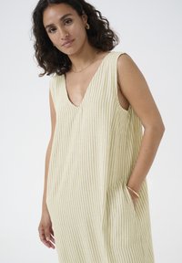 Robe sans manches à rayures de couleur jaune clair avec un profond décolleté en V. Elle possède des poches latérales et une coupe décontractée, fabriquée à partir d'un tissu doux.