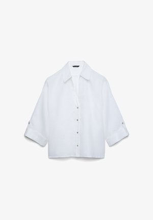 Chemise blanche à manches longues avec col large et manches retroussées aux trois quarts, présentée à plat sur un fond blanc.
