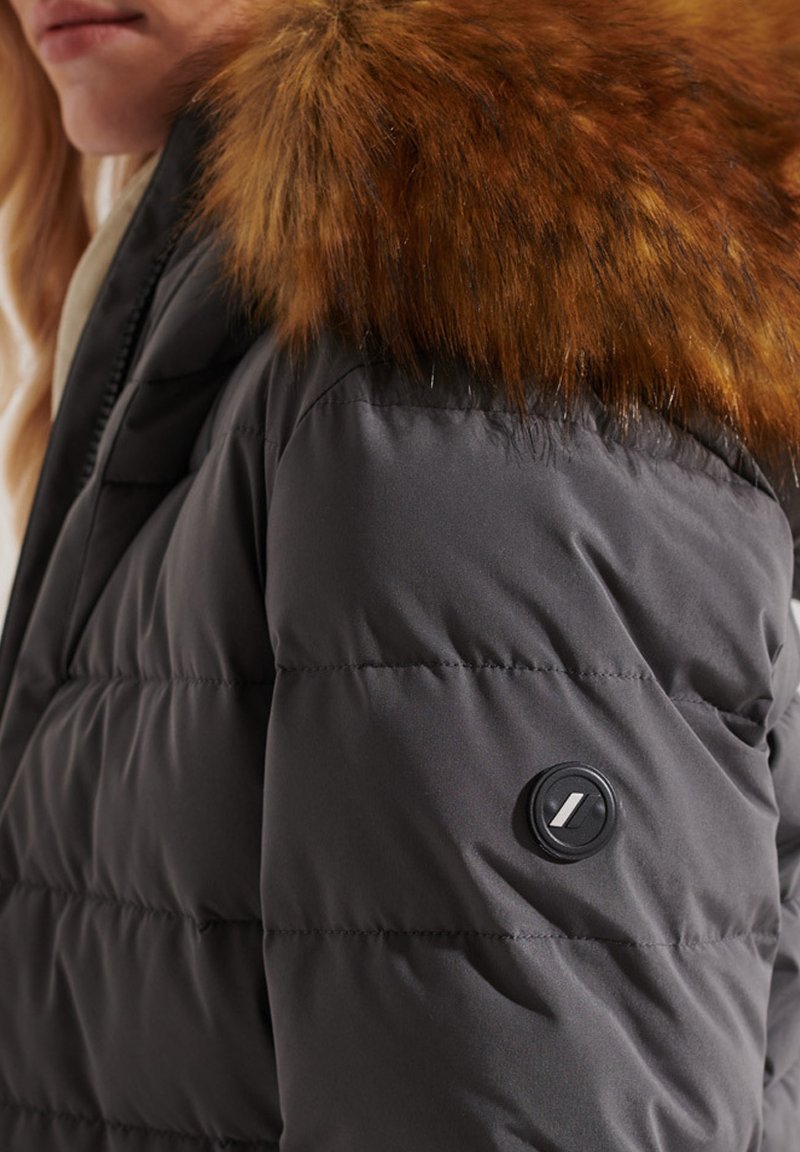 Grijs gewatteerd jack met een bruine bontkraag, featuring een ronde zwarte knoopdetails op de mouw en een gladde, glanzende stoftextuur.