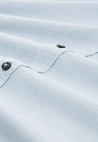 Helles blaues Gewebe mit kleinem strukturiertem Muster, das zwei schwarze Knöpfe auf einem gefalteten Bereich zeigt.