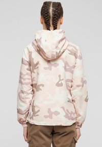 Kamouflagejacka i ljusrosa, beige och vitt. Har huva, elastiska ärmslut och en slät, glänsande yta med en avslappnad passform.