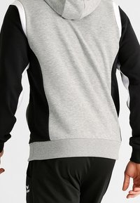 Felpa con cappuccio caratterizzata da un retro grigio, lati neri e dettagli bianchi. Realizzata in un tessuto morbido con polsini e orlo a coste.