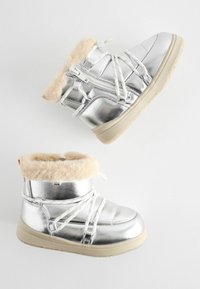 Silverfärgade metalliska ankelstövlar med fuskpälskrage, vita snören och en beige sula. Har en dragkedja och vadderad inredning för värme.