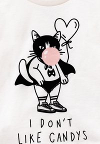 Gatto in bianco e nero in stile cartoon che indossa un mantello e scarpe da ginnastica, mentre soffia una gomma da masticare rosa e tiene in mano un palloncino a forma di cuore, con la scritta "Non mi piacciono le caramelle."