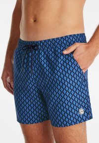Shorts de bain bleus à motif avec un design en diamant, taille élastique avec cordon de serrage et poches latérales. Accent de logo sur l'ourlet.