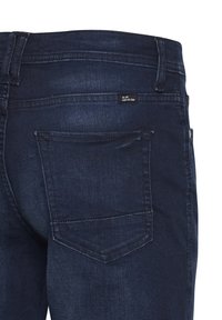 Sötétkék farmernadrág sima textúrával, hátul egy zsebbel, látható varrással és egy kis címkével a derékpántrész közelében.