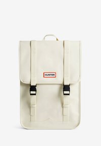 Sac à dos imperméable beige avec des bretelles réglables, des boucles noires et un grand rabat. Présente le logo "HUNTER" dans un cadre orange. Texture lisse.