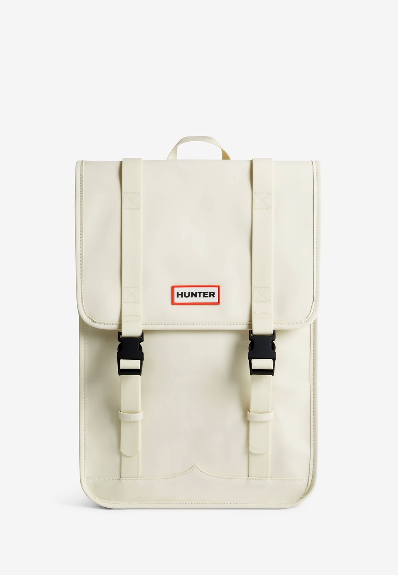 Sac à dos imperméable beige avec des bretelles réglables, des boucles noires et un grand rabat. Présente le logo "HUNTER" dans un cadre orange. Texture lisse.