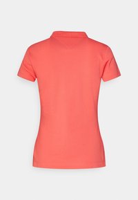 Koralli polo-paita, jossa on klassinen kauluspaita, lyhyet hihat ja sileä pinta; takana on V-muotoinen yksityiskohta.