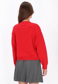 Czerwony sweter z dzianiny, okrągłym dekoltem, opadającymi ramionami i ściągaczami, w połączeniu z szarym spódnicą plisowaną. Miękka faktura.