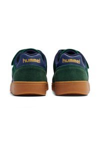 Sneakers in pelle scamosciata verde con tomaia in tessuto blu navy, suola in gomma color gomma e logo "hummel" dorato sul tallone. Lacci piatti e collarino imbottito.
