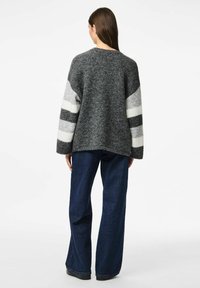 Maglione con un corpo grigio, vestibilità oversize e strisce a contrasto in grigio chiaro e nero sulle maniche. Abbinato a jeans blu a gamba larga.