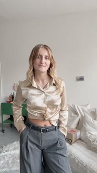 Satin beige blouse with a tie at the waist, paired with high-waisted gray trousers and a black belt. Simple design, subtle sheen.