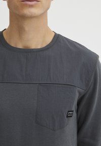 T-shirt in cotone grigio con pannello a contrasto, collo rotondo e taschino con etichetta del marchio. Texture liscia e design informale.