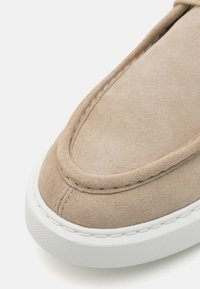 Beige semsket slip-on sko med rund tå, hevet søm og en hvit gummisåle med teksturert overflate.