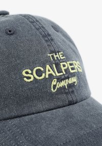 Gorra de color azul oscuro hecha de denim, con texto bordado en amarillo que dice "THE SCALPERS Company". Corona estructurada con visera curva.