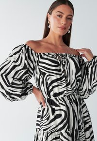 Schwarz-weiß gestreiftes Off-Shoulder-Kleid mit Puffärmeln, tailliertem Bund und einer Schleifen-detail am Ausschnitt.