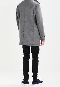 Šedý vlněný kabát s límcem, s jedním švem na zadní straně a knoflíkovými manžetami, v kombinaci s černými slim-fit kalhotami a námořnickými teniskami.