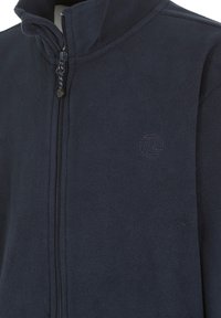 Marineblauwe fleecejack met hoge kraag, ritsluiting en subtiele logo borduring. Zachte textuur met een gladde, lichte stof.