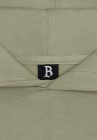 Sudadera de color verde oliva con un bolsillo frontal y una etiqueta negra con un logo blanco en el cuello. Tejido suave con un acabado texturizado.