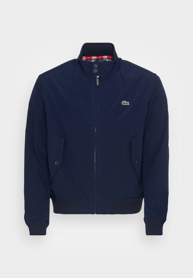 Veste bombers bleu marine avec un col montant, fermeture éclair, deux poches à rabat et doublure à carreaux. Présente un petit logo brodé sur la poitrine.