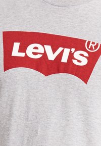 Camiseta gris con un gran logotipo rojo de Levi's, con texto en negrita en blanco en un diseño curvado. Tejido suave con un corte clásico de cuello redondo.
