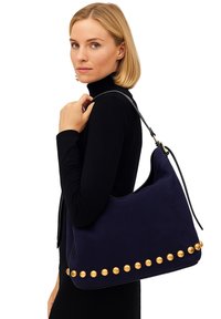 Borsa in suede blu navy con dettagli in metallo dorato lungo il fondo, dotata di una singola tracolla nera e un design arrotondato.