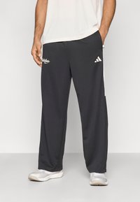 Fekete sportnadrág fehér Adidas logóval és oldalsávokkal, könnyű anyagból készült, kényelmes fazonú és egyenes szárú.