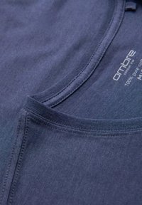 Tmavě modré bavlněné tričko s kulatým výstřihem a viditelnými švy. Štítek označuje 100% čistou bavlnu.