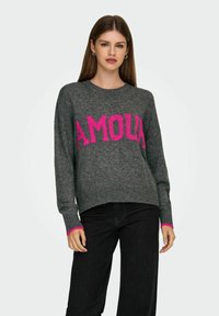 Suéter gris con un gráfico rosa de "AMOUR", puños acanalados con acentos rosas y un diseño de corte relajado. Combinado con jeans oscuros.