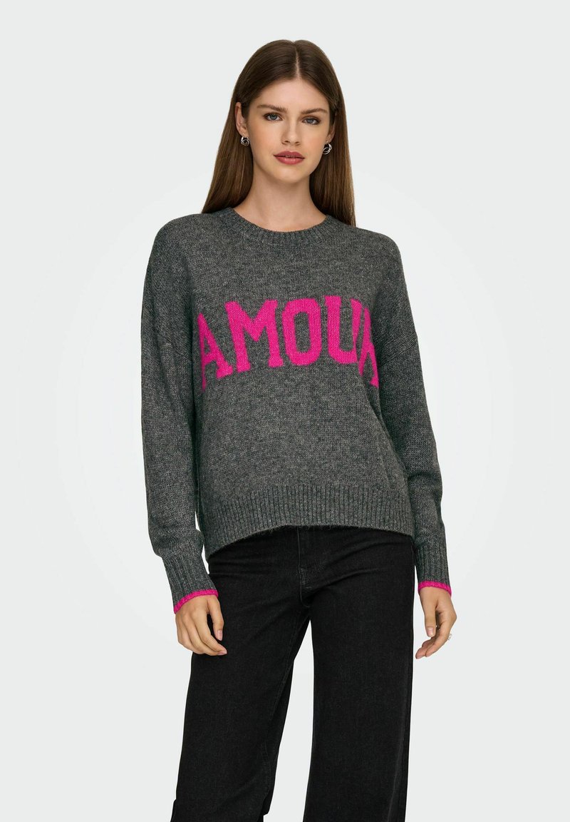 Suéter gris con un gráfico rosa de "AMOUR", puños acanalados con acentos rosas y un diseño de corte relajado. Combinado con jeans oscuros.