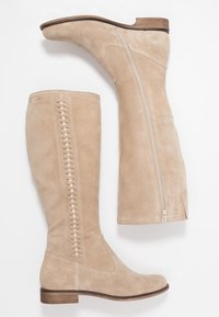 Bottes hautes jusqu'au genou en daim beige avec une fermeture éclair latérale et un détail de laçage décoratif. Talon en bois empilé, texture lisse et design élégant.