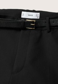 Pantalons noirs avec une ceinture texturée noire ornée d'une boucle dorée et d'une étiquette de taille MNG blanche visible à l'intérieur de la taille.