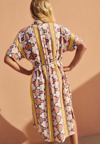 Kaftan multicolore con maniche corte, caratterizzato da design geometrici in arancione, giallo e blu su un tessuto leggero. Legato in vita.