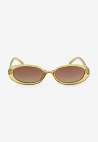 Ovale zonnebril met een gouden kunststof frame en bruine gradient glazen. Het ontwerp heeft vloeiende contouren en slanke pootjes.