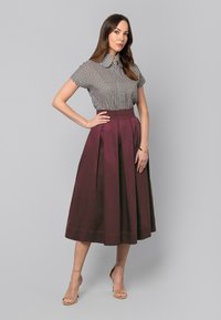 Czarna i biała bluzka w wzór houndstooth z krótkimi rękawami, zestawiona z bordową, plisowaną spódnicą midi. Neutralne sandały na paski dopełniają całość.