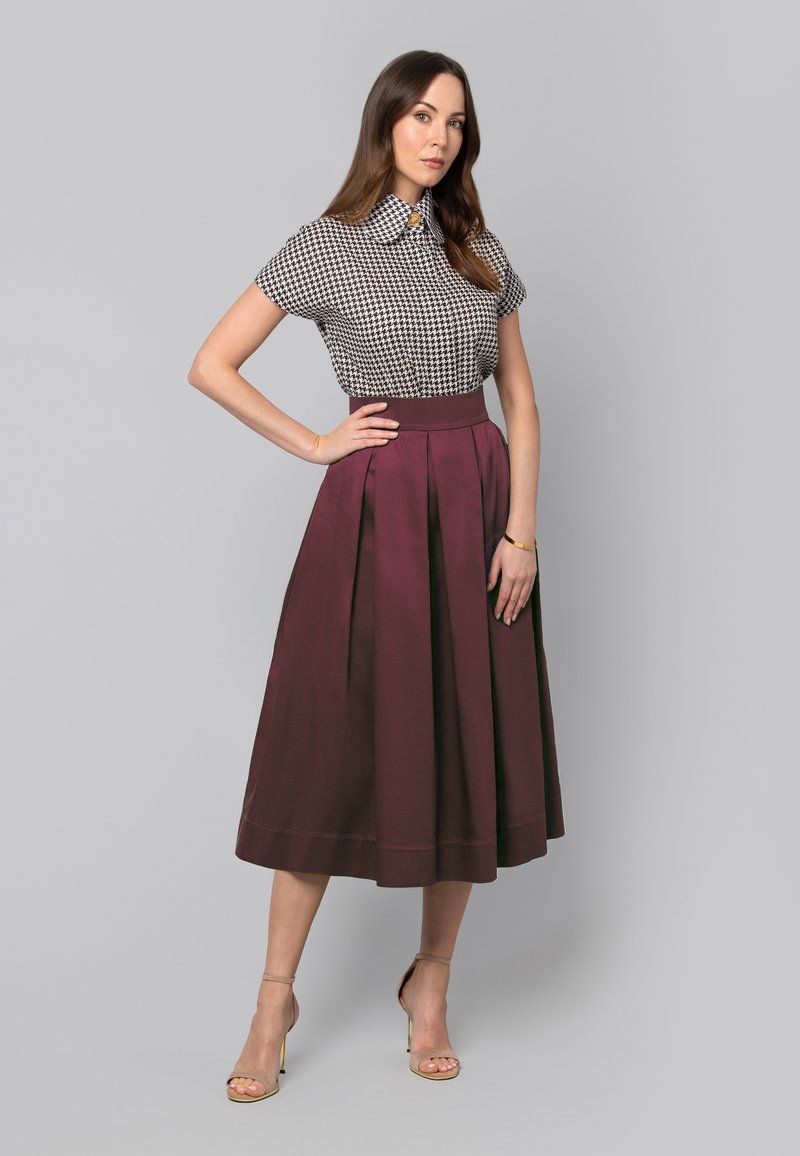 Czarna i biała bluzka w wzór houndstooth z krótkimi rękawami, zestawiona z bordową, plisowaną spódnicą midi. Neutralne sandały na paski dopełniają całość.