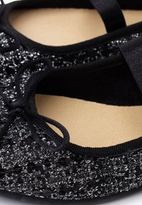 Ballerine nera con tessuto testurizzato e fili metallici. Design a punta chiusa con fiocco decorativo e morbida fodera interna.