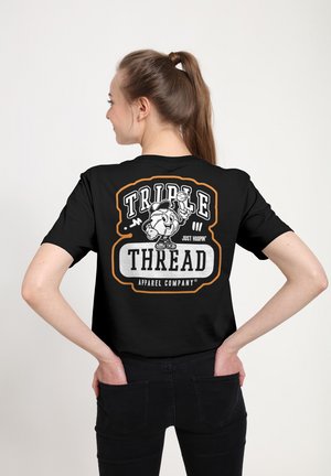 Kvinde med brunt hår i hestehale iført sort t-shirt med tegneserie basketballfigur og teksten "Triple Thread Apparel Company" på ryggen.