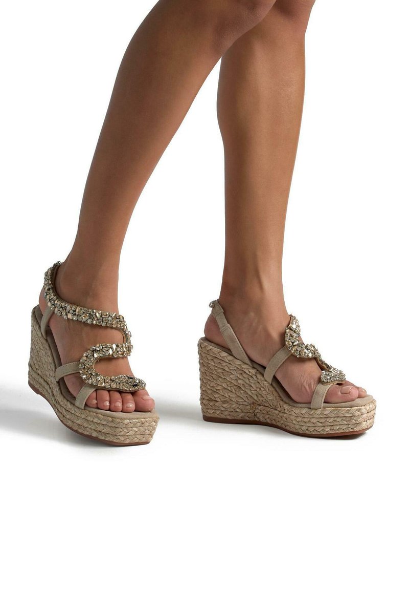 Sandali con zeppa beige con base in espadrilles, caratterizzati da un accento decorativo di perline sulla strap. Punta aperta e cinturino alla caviglia regolabile.