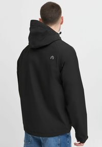 Črna jakna s kapuco, izdelana iz gladkega, lahkega materiala. Ima subtilen logo na hrbtu in sproščen, ohlapen kroj.