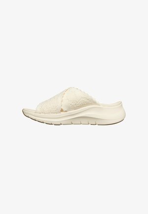 Sandale blanche à enfiler avec des brides croisées en maille texturée et une semelle coussinée, vue de profil sur un fond uni.