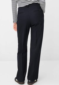 Marineblauwe broek van een gladde stof met een rechte snit, twee achterzakken en een elastische tailleband. Gecombineerd met donkere schoenen.