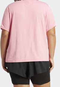 Camiseta de manga corta de color rosa claro con un ajuste relajado, hecha de tejido suave; llevada sobre pantalones cortos negros en capas. Diseño sencillo, sin patrones ni acentos.