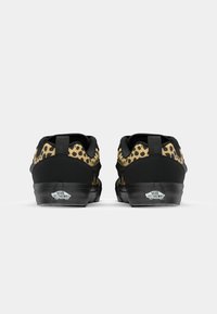 Svart sneakers med leopardmønsterdetaljer, med en glatt tekstur, flatt design og Vans-logo på hælen. Kompakt og uformell stil.
