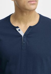 Námornícky modré tričko henley vyrobené z jemnej bavlny, s dvomi gombíkmi a kontrastným svetlomodrým akcentom a zaobleným výstrihom.